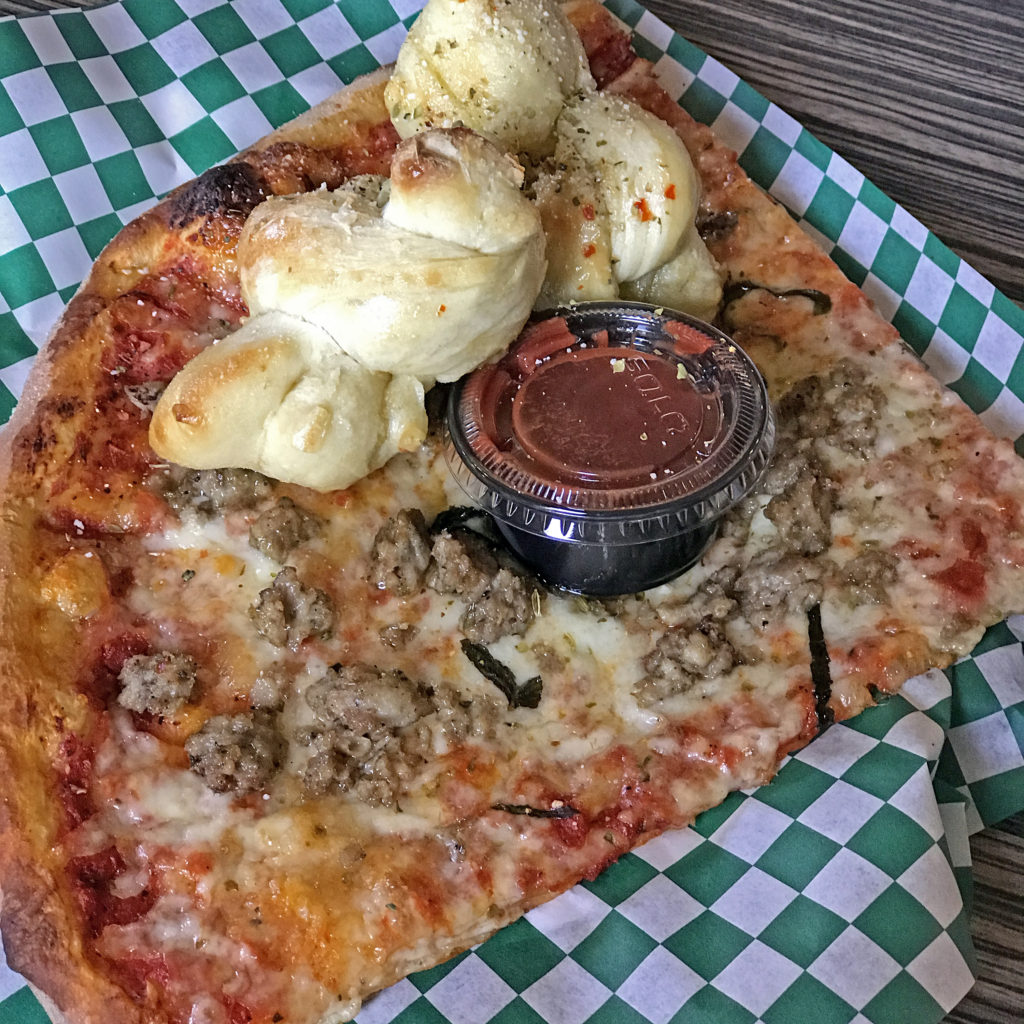 An oversize slice topped with house-made sausage and a couple of garlic knots at Butchertown Pizza Hall.