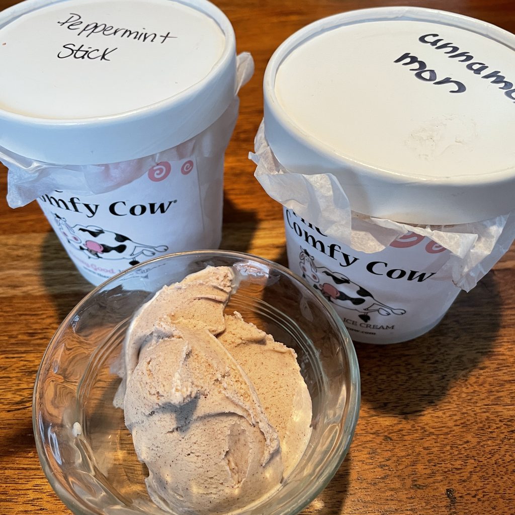 Pints of Comfy Cow peppermint stick and cinnamon mon ice cream flank a scoop of cinnamon mon.