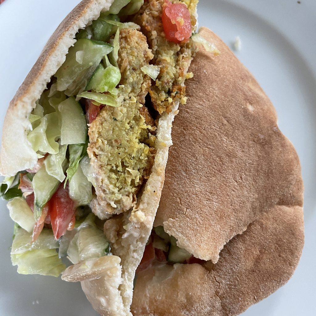 We've carved an Alwatan falafel in half to display its generous filling of tender falafel balls, lettuce, tomato, and creamy tzatziki sauce in a fresh, tender pita.