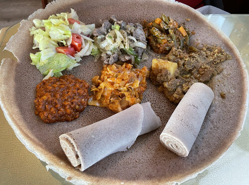 The filling combination tips plate features two beef dishes, three veggie items, and a tasty American-style salad, all served on a plate-size injera base.